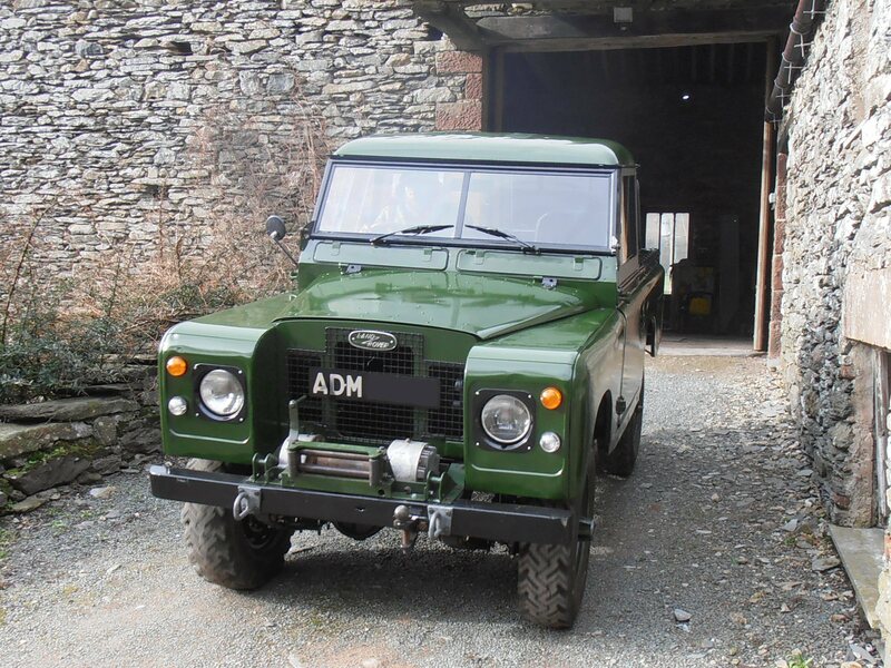 Green Land Rover Series 2a front view on drive in front of open barn door.